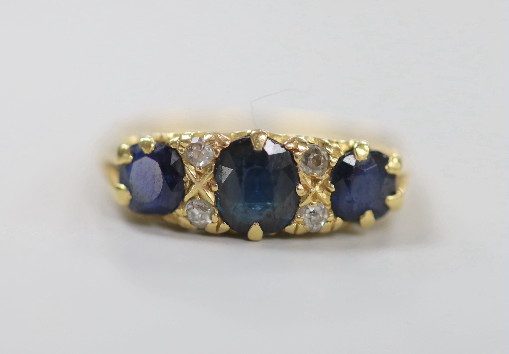 An early to mid 20th century gold, three stone sapphire and four stone diamond chip set half hoop ring, size O, gross weight 4.5 grams.